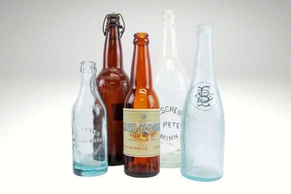 Hero image of clear, aqua, and brown glass bottles of varying sizes for an upcoming exibit about bottling and brewing soda and beer in Nicollet County