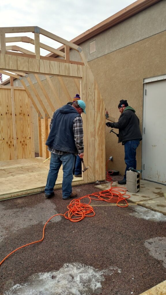 Color photo of a group of three adult males working to build a utility shed
