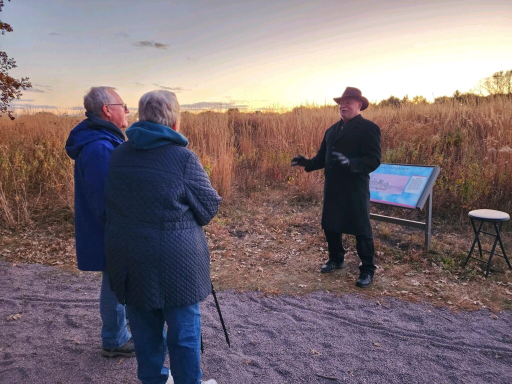 A man in a coat on a trail talking to two adults.