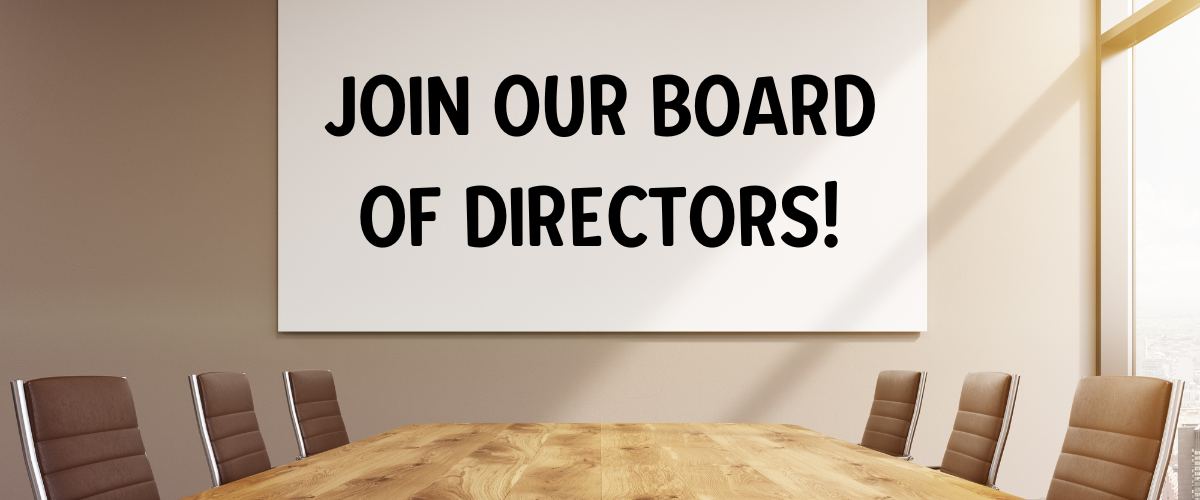 Conference room with a large wooden table and several chairs; a sign on the wall reads, "Join our Board of Directors!" in bold black letters. Sunlight enters from a window on the right.