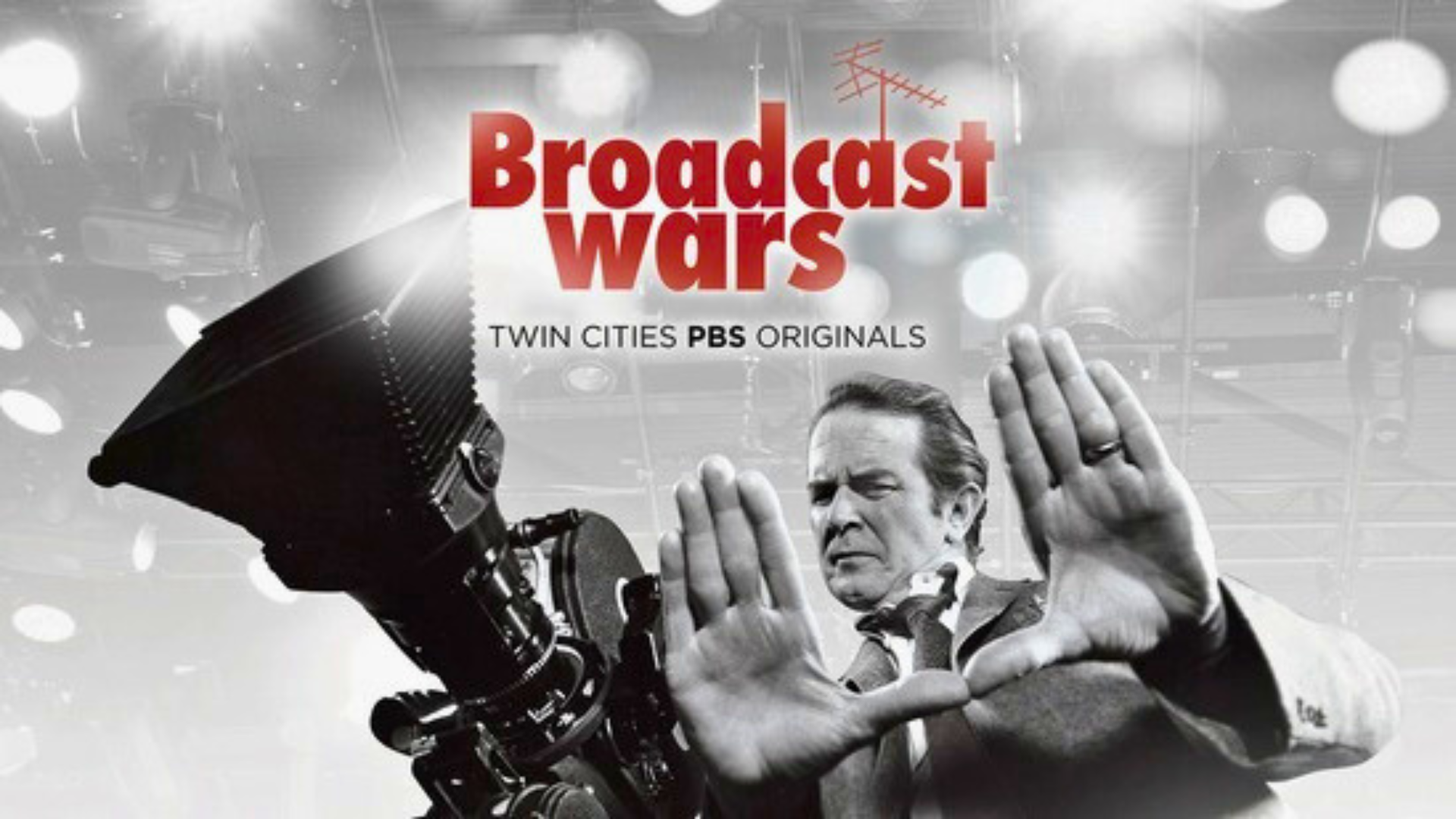 A man stands behind a large studio camera, framing a shot with his hands. The text "Broadcast Wars, Twin Cities PBS Originals" appears above him on a background of lights and equipment.