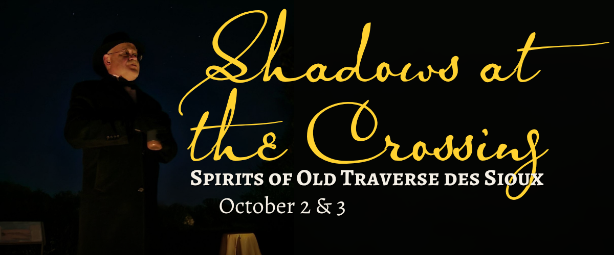 A person stands outdoors at night with arms crossed, illuminated by soft light. The text reads, “Shadows at the Crossing: Spirits of Old Traverse des Sioux, October 2 & 3.”.
